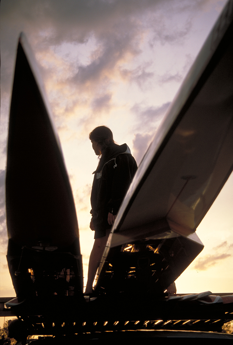 Woman by racing shells at sunrise