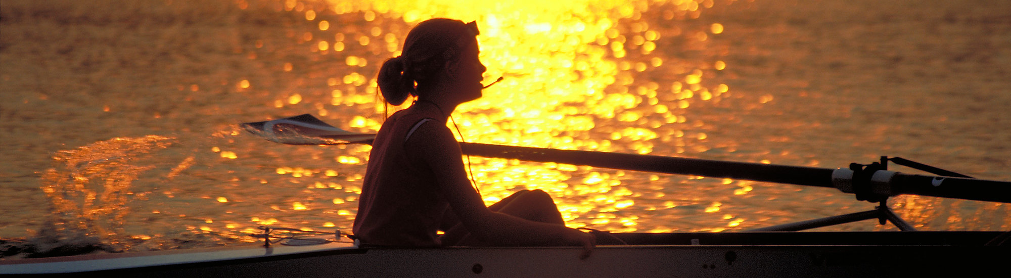 Rowing coxwain in boat at sunset on lake